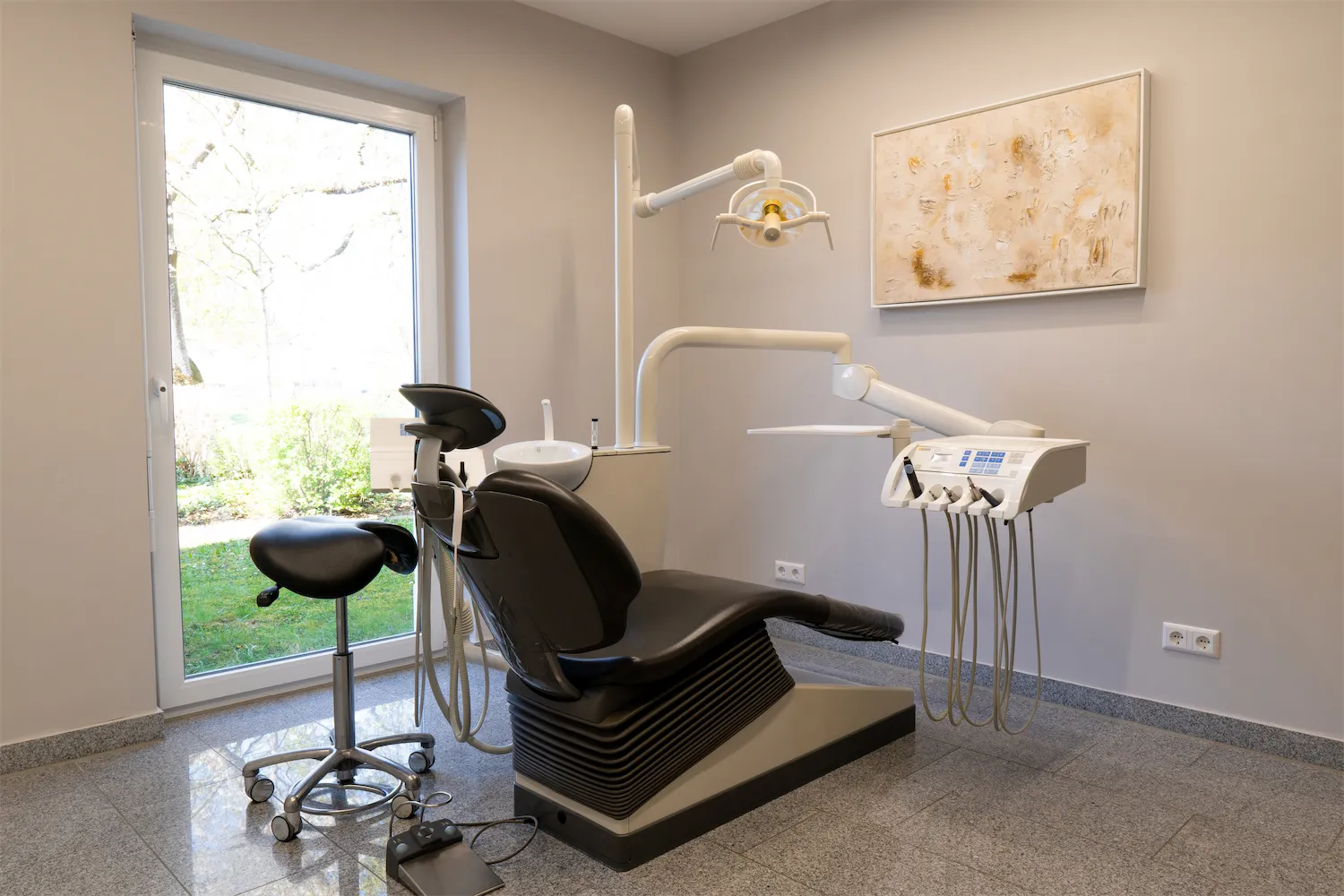 Behandlungszimmer mit Behandlungsstuhl, Wandbild und Fenster zum Garten