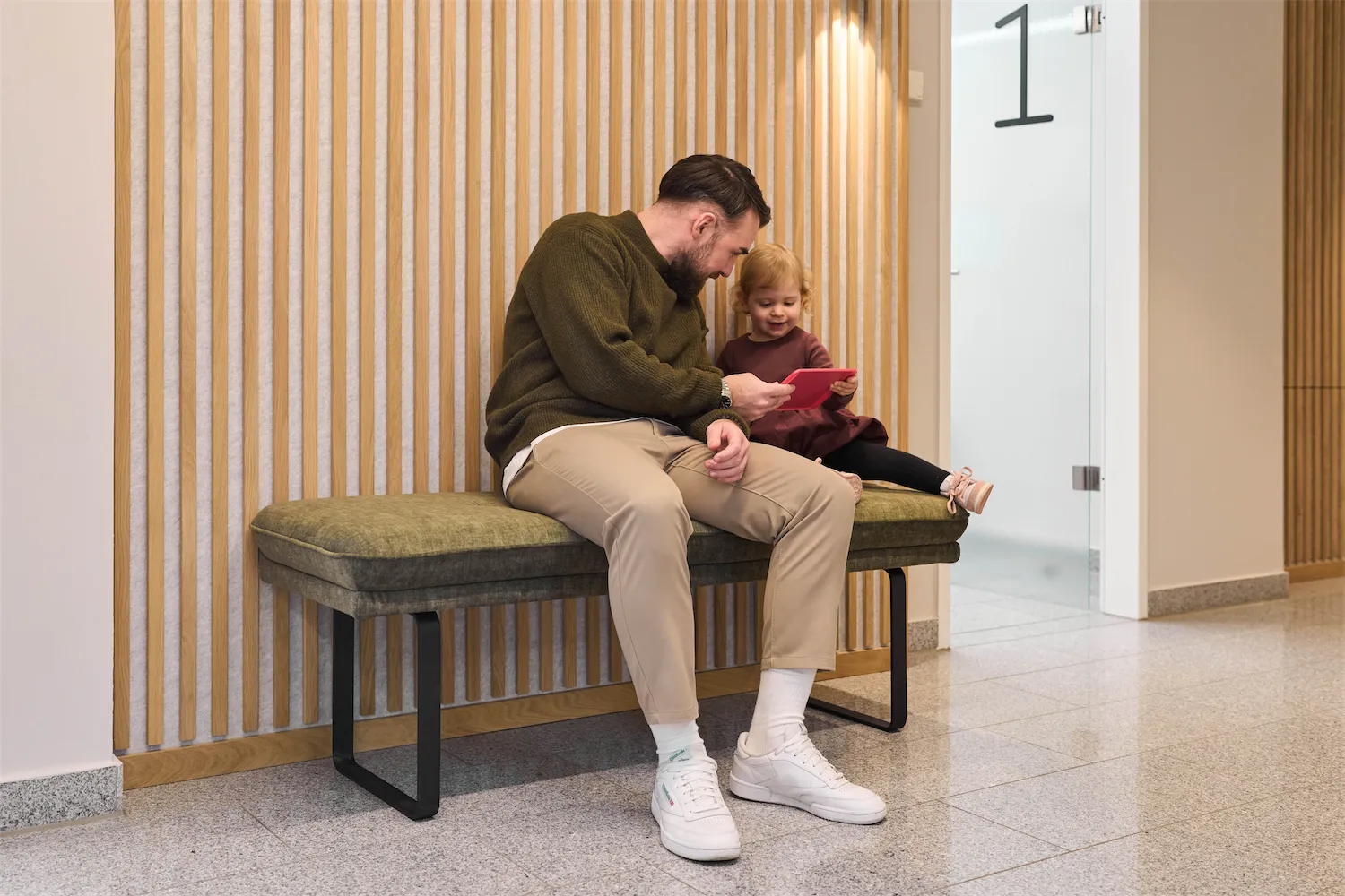 Vater und Kind warten auf einer Bank im Flur