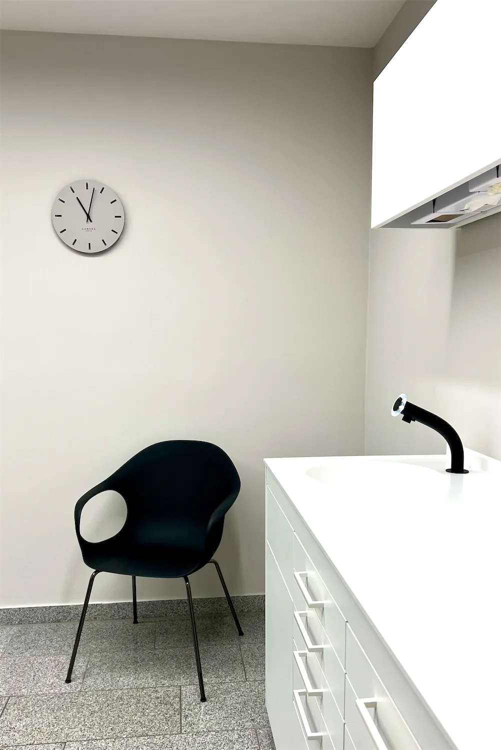 Raum mit Stuhl, Waschbecken und Wanduhr
