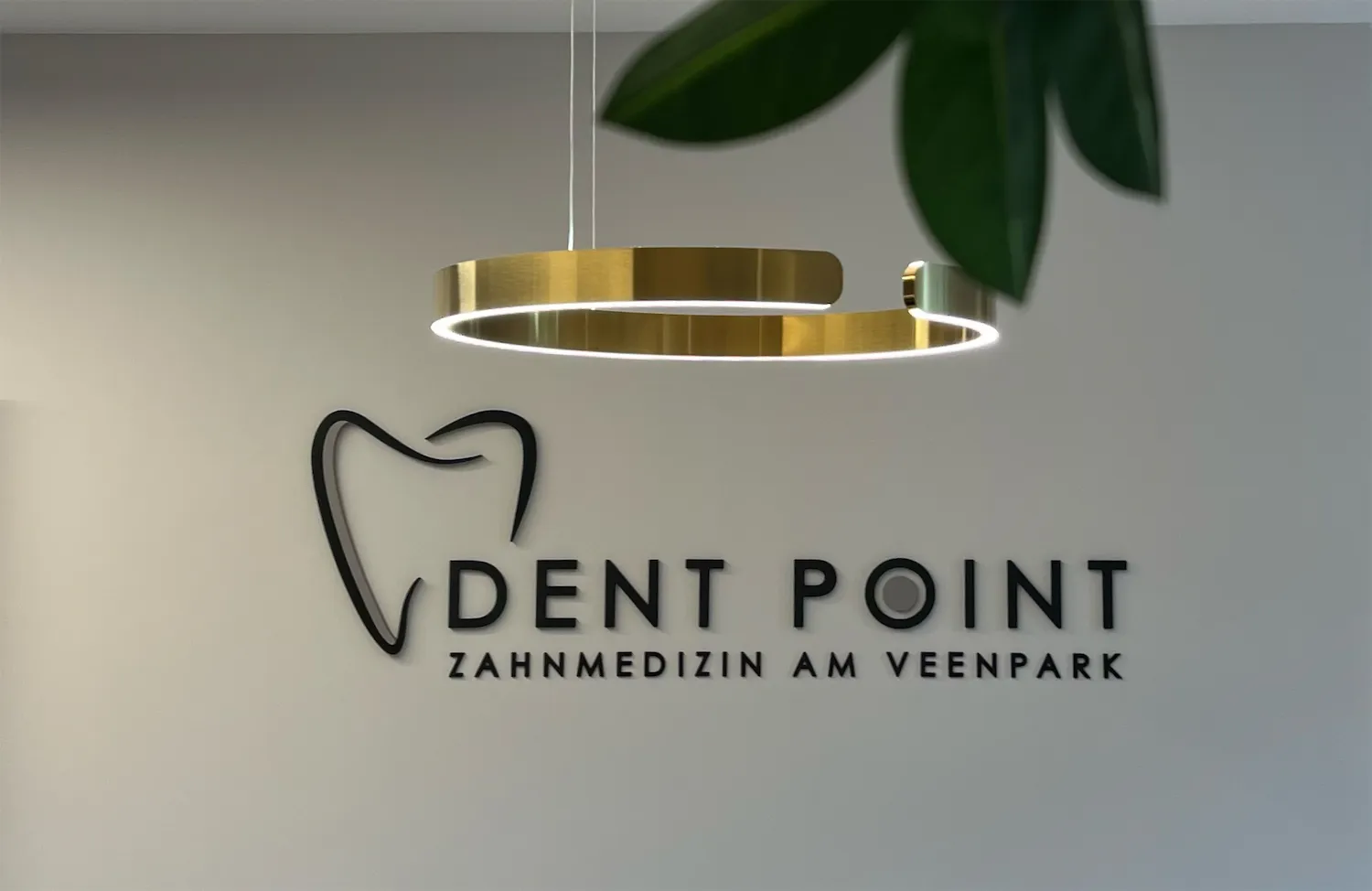 Praxislogo „Dent Point – Zahnmedizin am Veenpark“ an der Wand unter einer goldenen Ringleuchte