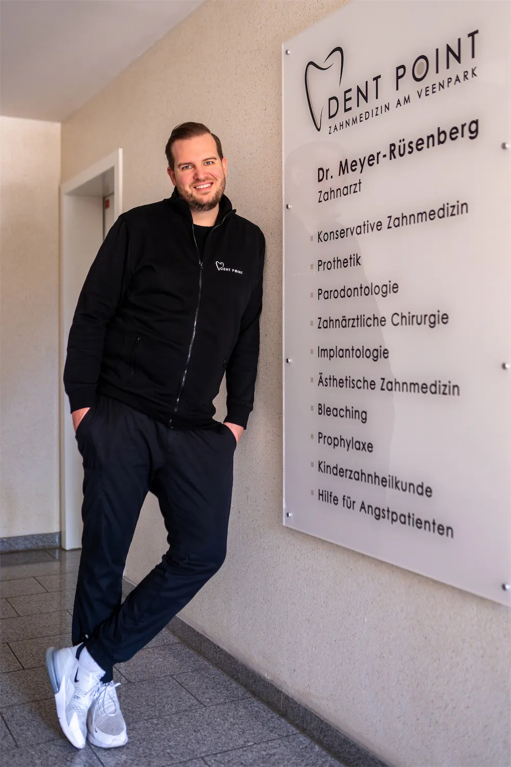 Zahnarzt neben dem Praxisschild mit den Leistungen der Praxis